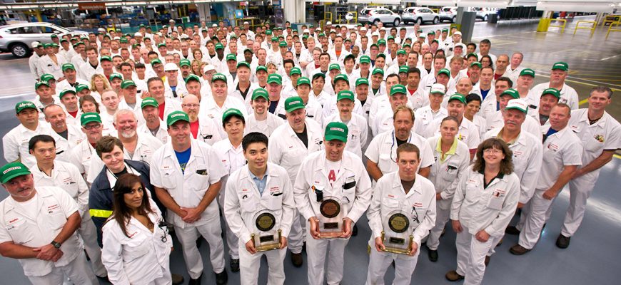 Honda factory employees with green hats pose for a picture holding three awards